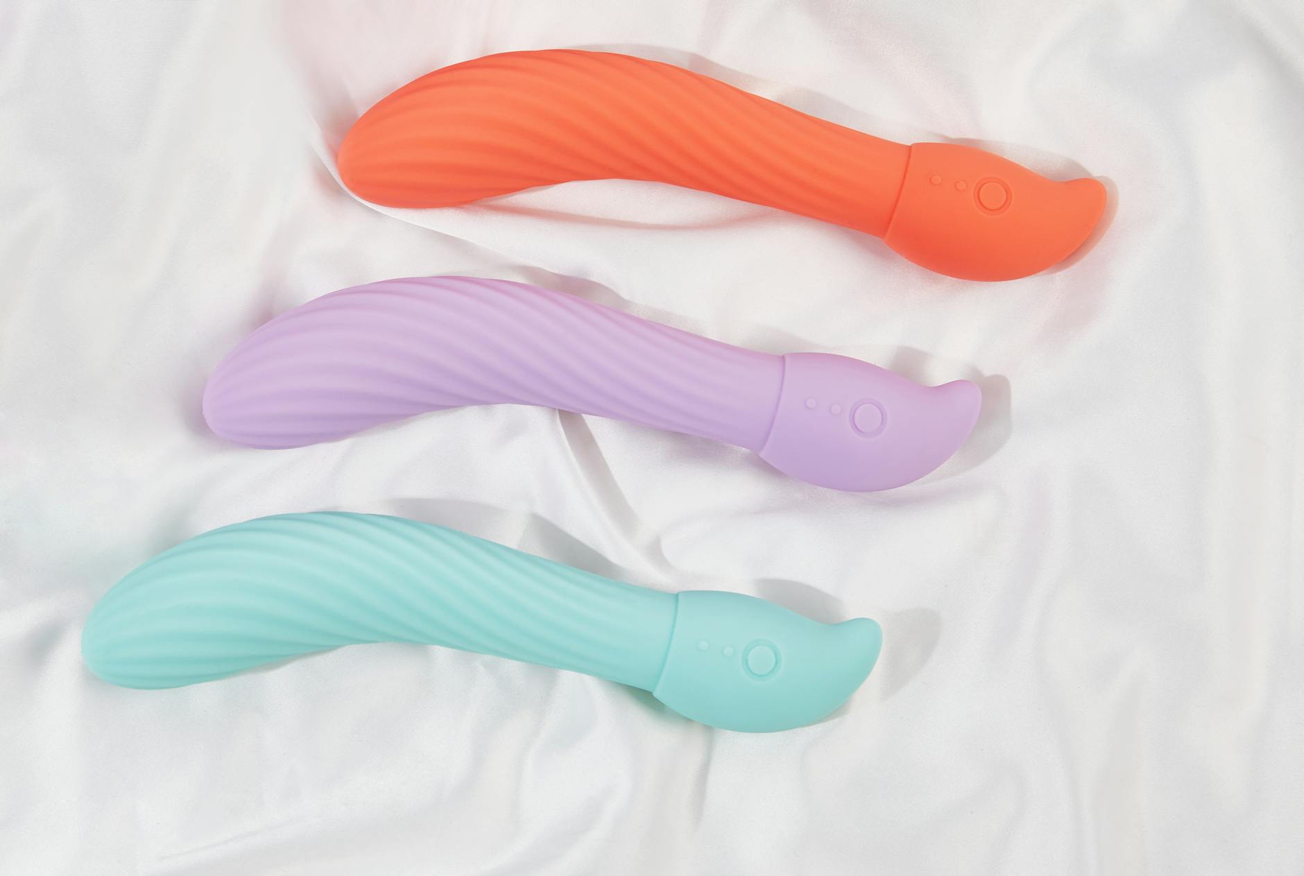 Three colorful clitoral vibrators arranged on white fabric, highlighting smooth texture and design.