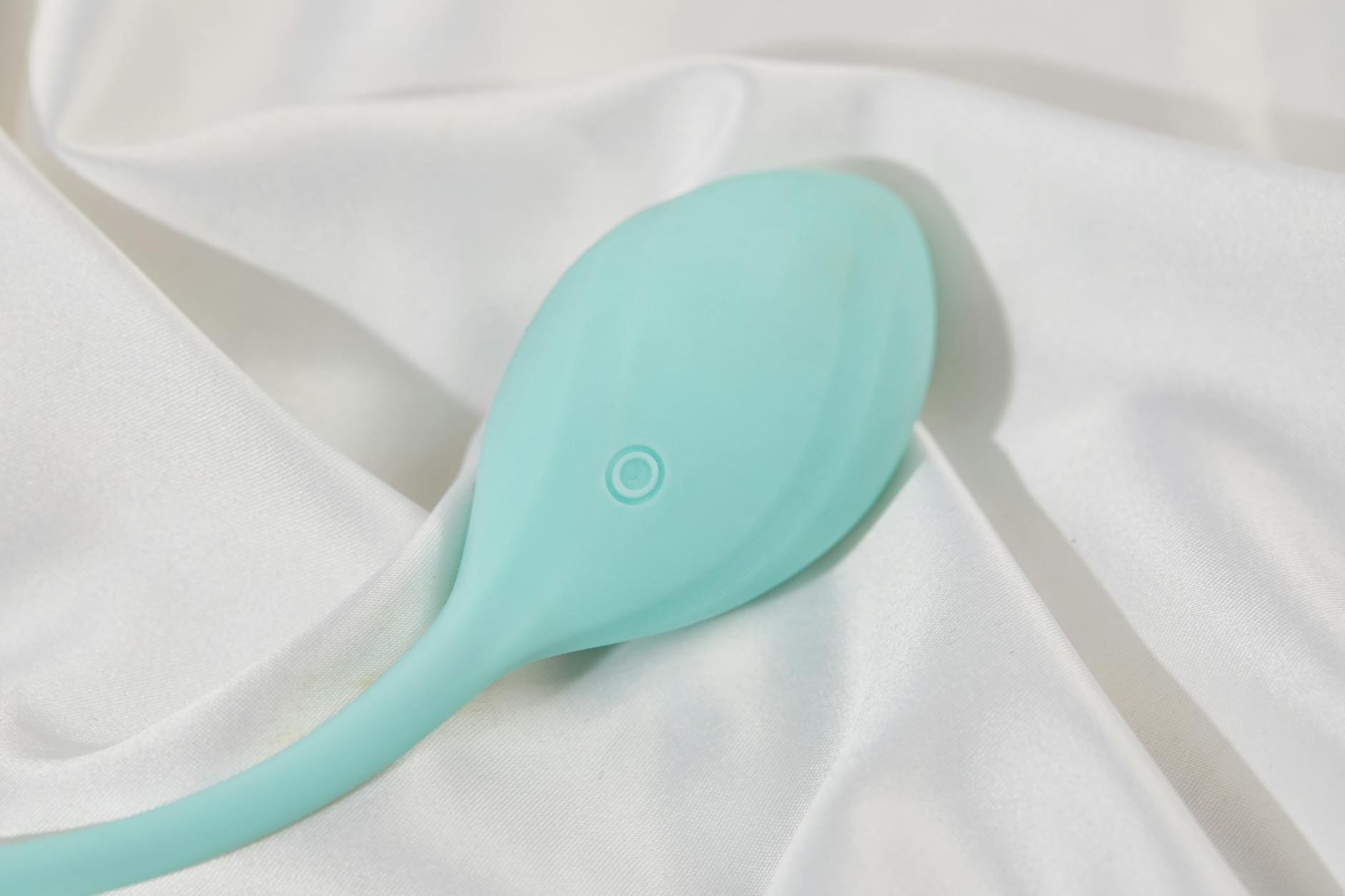 A teal lemon vibrator resting on soft white silk fabric, symbolizing gentle pleasure after hormonal transitions.