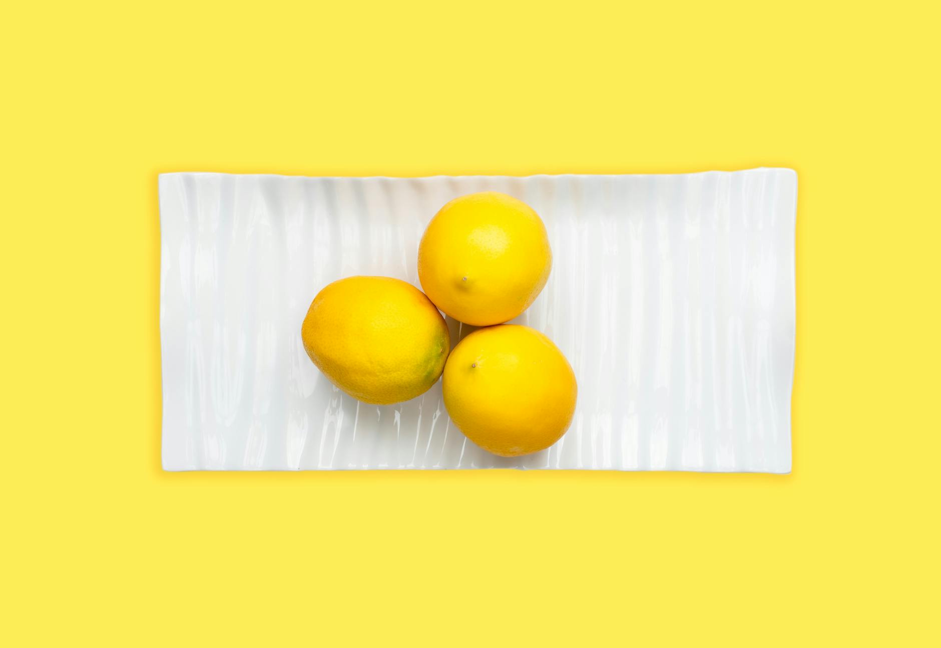 Fresh lemons arranged on a white plate with yellow background, representing the refreshing sensation of pain-free pleasure