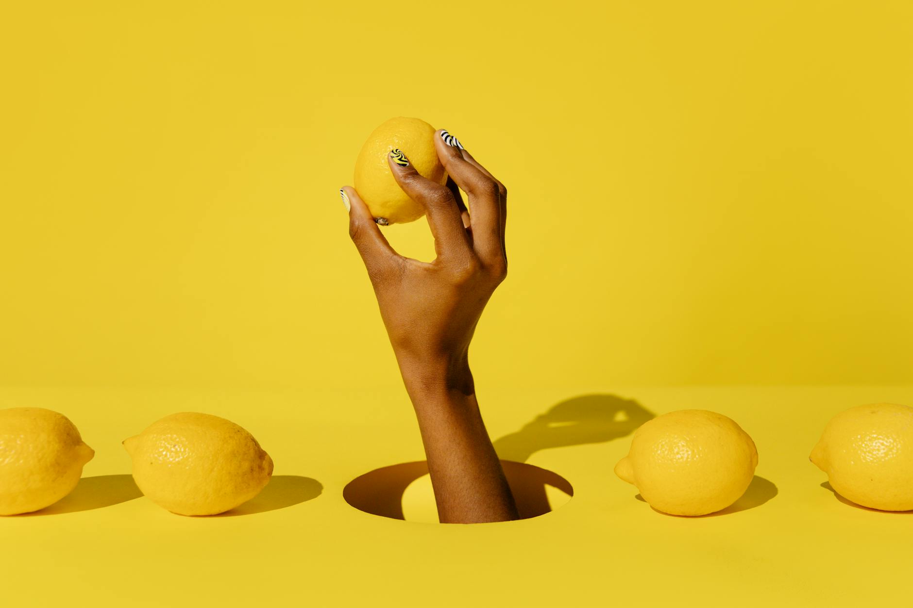 A hand holding a fresh lemon against a bright yellow background, symbolizing heightened sensitivity and refreshed sensation