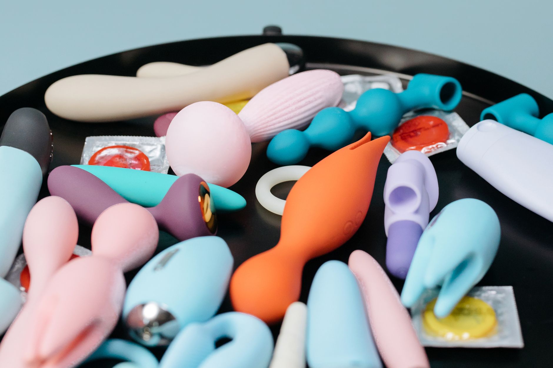 Two hands holding vibrators against a pastel background