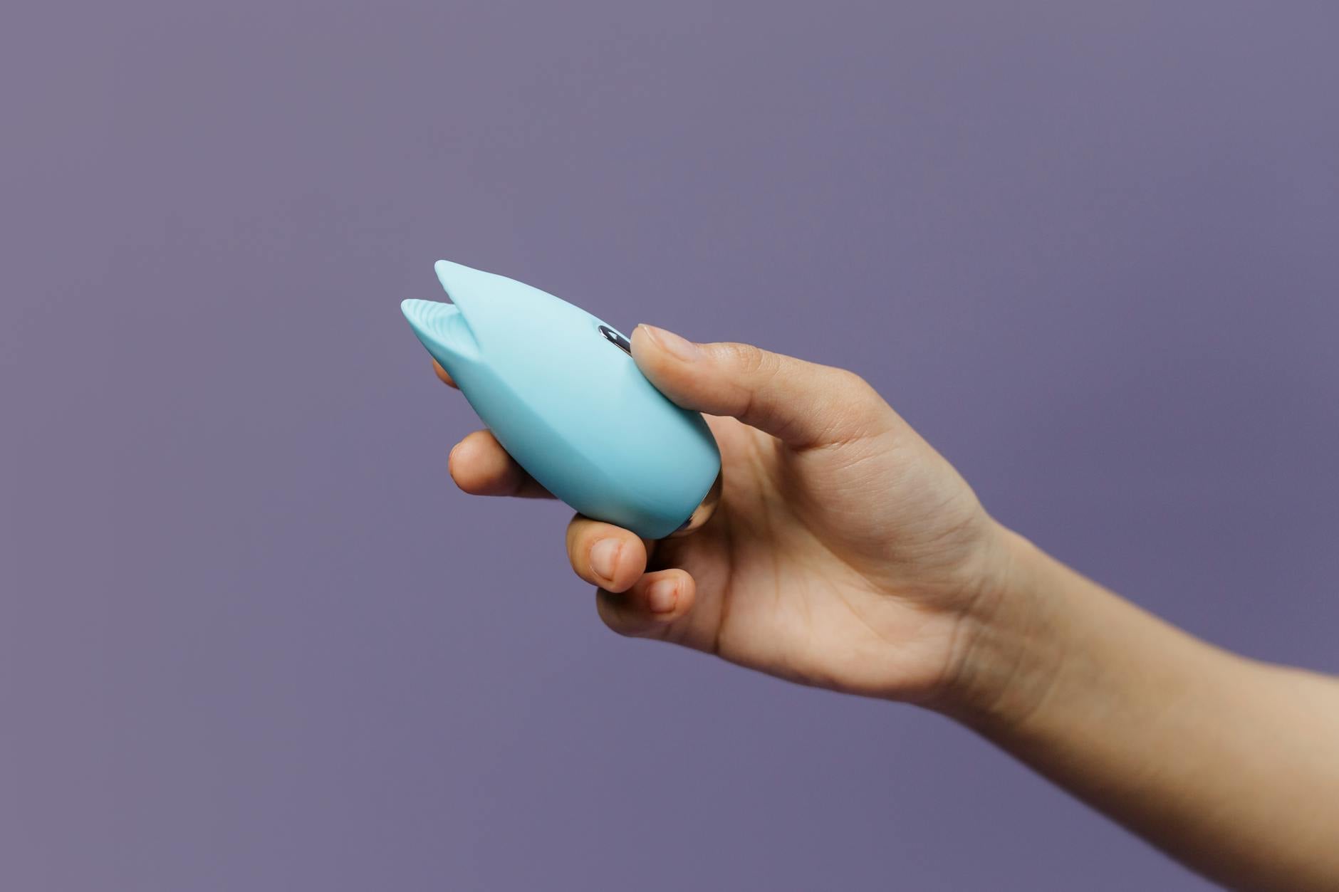 A blue lemon clitoral vibrator held gently in hand against a purple background, promoting self-care and wellness